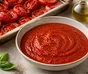 Schale mit glatter roter Tomatensauce, umgeben von gerösteten Tomaten, Knoblauch und Basilikum